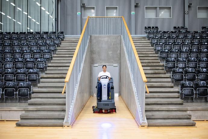 Floor scrubber cleaning concourse and seating areas inside a stadium environment.