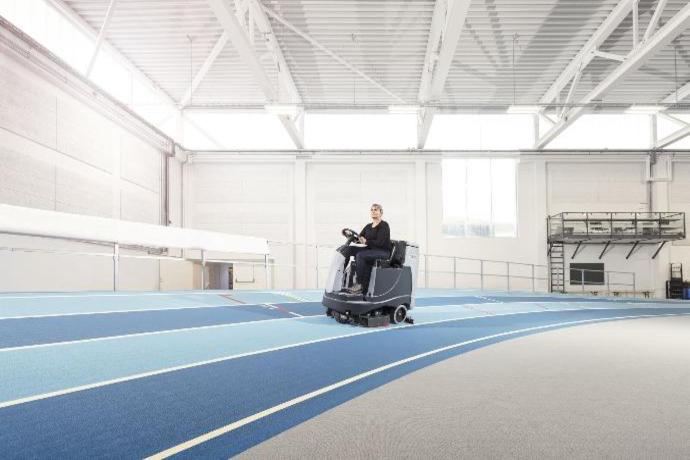 Ride-on scrubber machine cleaning an indoor athletics track